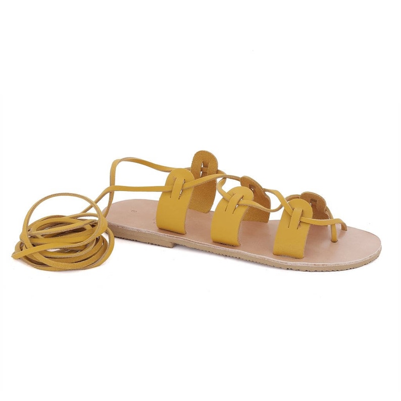 May include: Yellow leather sandals with laces that tie up the leg. The sandals have a flat sole and are made of a soft, supple leather.