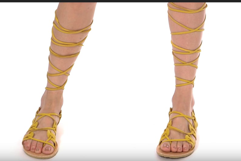 May include: A pair of yellow leather sandals with laces that wrap up the legs. The sandals have a simple design with a flat sole.
