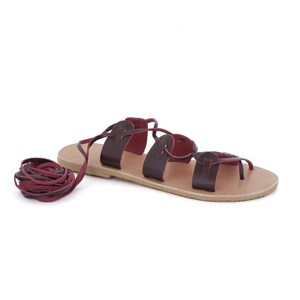 May include: Brown leather sandals with a burgundy leather lace-up closure. The sandals have a flat sole and a simple design.