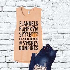 Op de afbeelding: Een perzikkleurig tanktop zonder mouwen met de tekst "Flannels Pumpkin Spice Hayrides S'mores Bonfires" erop gedrukt. De tekst is zwart met een kleine oranje pompoenafbeelding en een hartje.