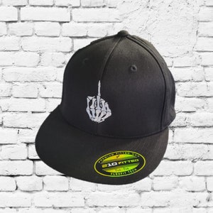 Op de afbeelding: Zwarte, getailleerde baseballpet met een witte skelethand die de middelvinger opsteekt. De pet heeft een groen-geel label met de tekst "Premium Fitted Cap 210 Fitted 7 1/4 - 7 3/8 Flexfit Tech".
