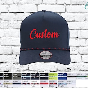 May include: A navy blue trucker hat with a red rope trim and a white label that says "Imperial True Fit". The hat has the word "Custom" written in red cursive on the front.
