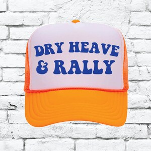 May include: A trucker hat with a white front panel and orange brim and mesh. The text "DRY HEAVE & RALLY" is printed in blue on the front panel. The hat has a curved brim and an adjustable snap closure.