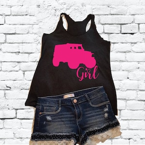 May include: A black tank top with a pink silhouette of a truck and the word "Girl" printed on it. The tank top is paired with denim shorts.