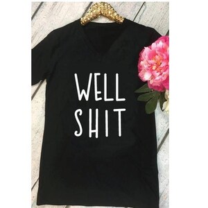 May include: Black v-neck t-shirt with the text "WELL SHIT" printed in white.