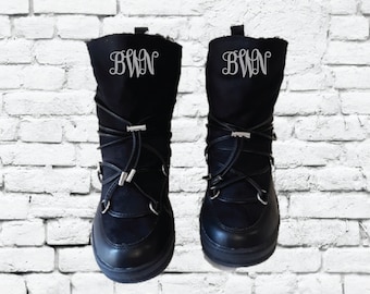 Op de afbeelding: Een paar zwarte winterlaarzen met een wit monogram dat "BWN" op elke laars staat.