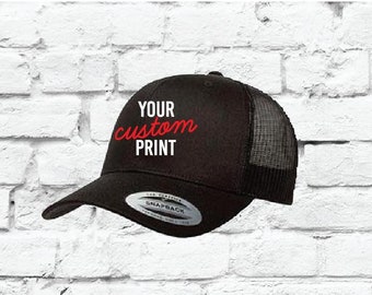 May include: Black trucker hat with a black mesh back. The hat has a red embroidered design that says "YOUR custom PRINT".