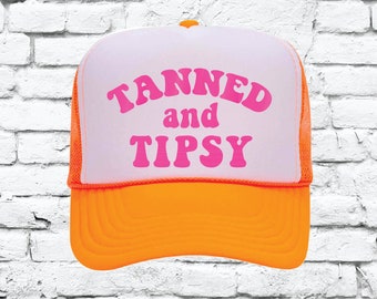 May include: A white and orange trucker hat with the text "TANNED and TIPSY" in pink letters.