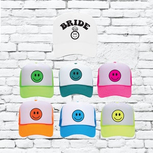 May include: Seven trucker hats with a white front and a mesh back. The front of each hat features a smiley face in a different color. One white hat has the word "BRIDE" in black letters with a diamond ring and smiley face.