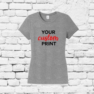 Könnte beinhalten: Ein hellgraues T-Shirt mit kurzen Ärmeln und Rundhalsausschnitt. Das Shirt trägt den Text "YOUR custom PRINT" in schwarzer und roter Schrift.