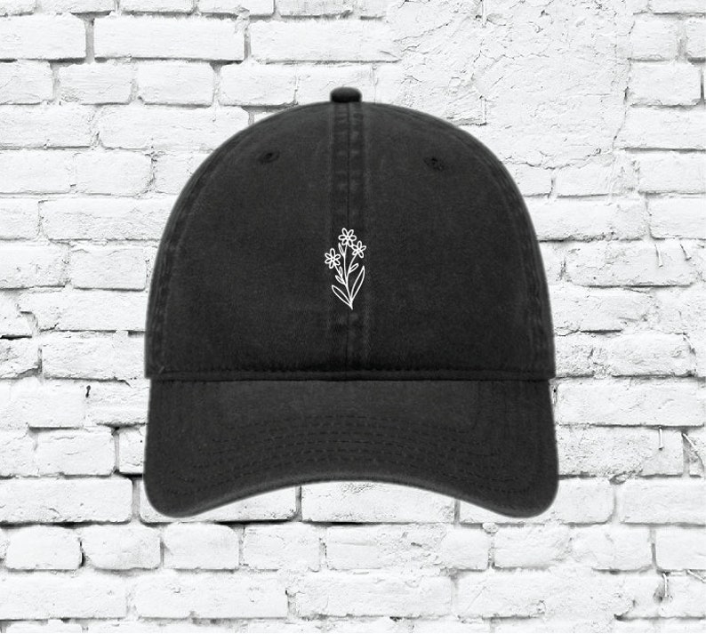Puede incluir: Una gorra de b&eacute;isbol negra con un dise&ntilde;o de flor bordado en blanco.