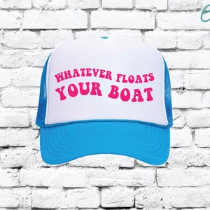 May include: A white trucker hat with a blue mesh back. The front of the hat has the text "Whatever Floats Your Boat" in pink letters.