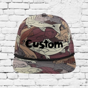 Op de afbeelding: Een zwarte en bruine baseballpet met een aangepast ontwerp met een patroon van vissen. De tekst "Custom" is in zwart op de voorkant van de pet gedrukt.