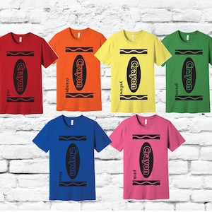 May include: A selection of short-sleeved t-shirts in a range of colours, each displaying a crayon design. The shirts are red, orange, yellow, green, blue, and pink, with the word "Crayon" and the colour name printed on each.