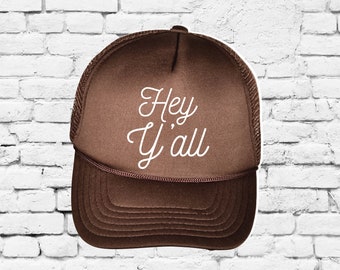 May include: Brown trucker hat with a white embroidered design that says "Hey Y'all".