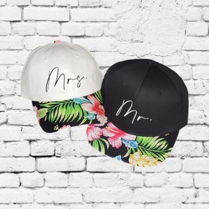 May include: Two baseball caps with floral print brims. One cap is white with the word "Mrs." embroidered in black. The other cap is black with the word "Mr." embroidered in white.