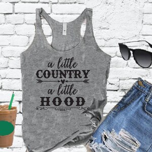 Puede incluir: Una camiseta sin mangas gris con el texto "a little COUNTRY a little HOOD" impreso en ella. El texto está en negro e incluye un pequeño corazón y flechas.