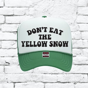 Può includere: Cappellino da camionista verde e bianco con la scritta "DON'T EAT THE YELLOW SNOW" in nero. Il cappellino ha una visiera verde e un pannello frontale bianco con retro in rete. L'etichetta dice "OTTO WORLD FAMOUS FOR COMFORT TRUCKER".