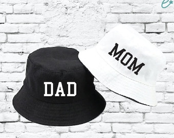 May include: Two bucket hats, one black with the word "DAD" in white letters and one white with the word "MOM" in black letters.