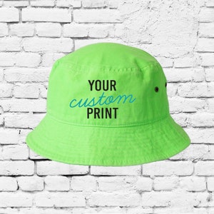 Puede incluir: Un gorro de cubo verde brillante con texto negro que dice "YOUR custom PRINT" en la parte delantera.