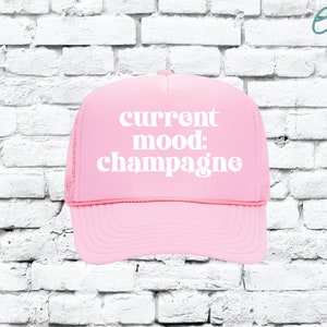 May include: Pink trucker hat with white text that reads "current mood: champagne".