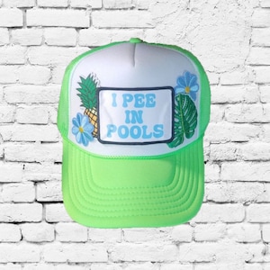 Puede incluir: Una gorra de camionero verde neón con una malla blanca en la parte posterior. La parte delantera de la gorra presenta un parche blanco con el texto "I PEE IN POOLS" en letras azules. La gorra está decorada con una piña, una flor azul y una hoja verde.