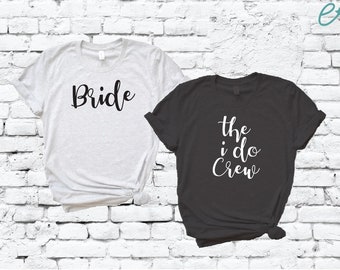 May include: Two t-shirts, one white and one black, with text printed on them. The white t-shirt says "Bride" in black script. The black t-shirt says "the i do Crew" in white script.