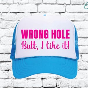 May include: A trucker hat with a white front panel and a blue brim and mesh back. The hat features the text "WRONG HOLE Butt, I like it!" in bright pink lettering.