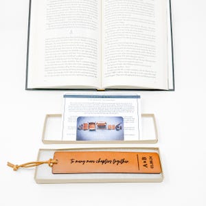 An open book with text on the pages, a brown leather bookmark with text, and a box containing a card with a graphic design.