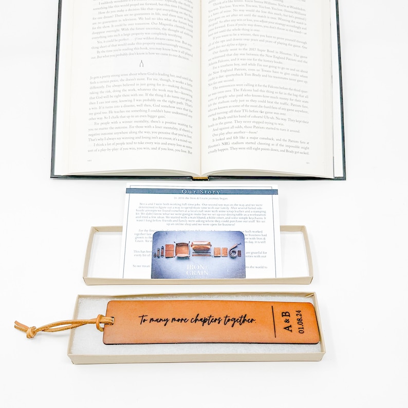An open book with text on the pages, a brown leather bookmark with text, and a box containing a card with a graphic design.