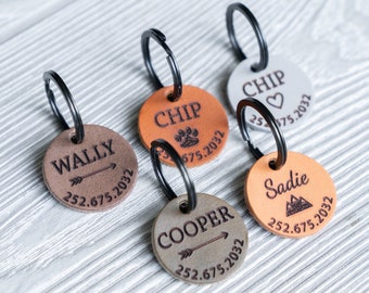 May include: Five leather dog tags with key rings. The tags are brown, tan, and gray. Each tag has a different name engraved on it, including Wally, Chip, Cooper, Sadie, and Chip. The tags also have a phone number and year engraved on them.