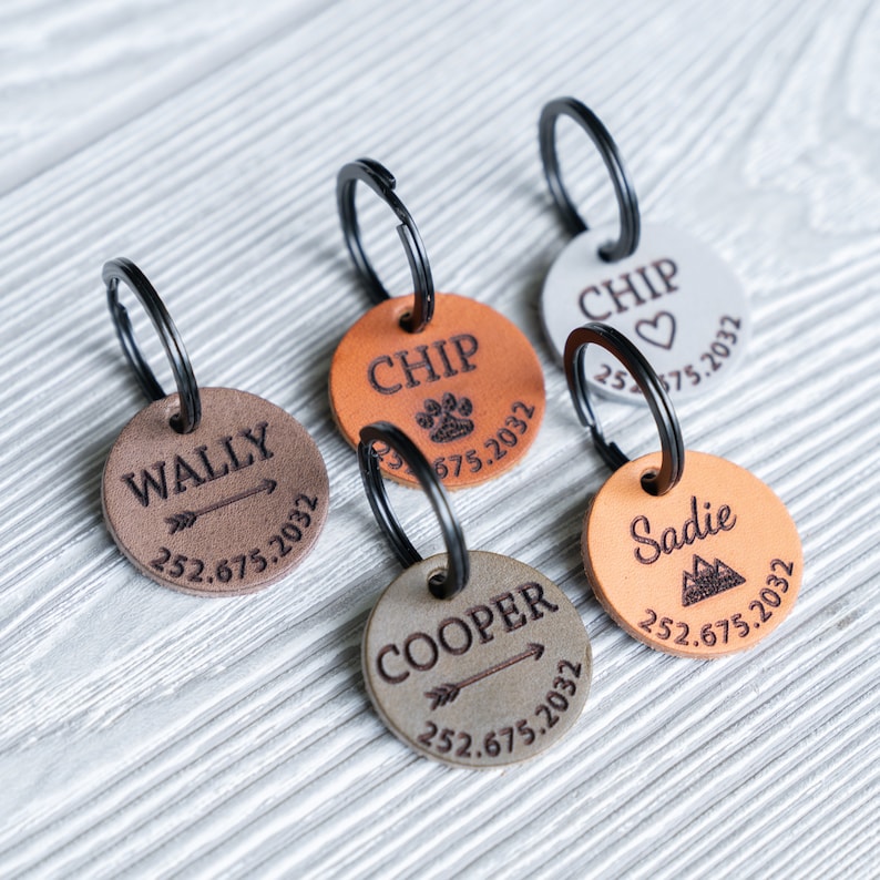 Puede incluir: Cinco chapas de perro de cuero con llaveros. Las chapas son marrones, beige y grises. Cada chapa tiene un nombre diferente grabado, incluyendo Wally, Chip, Cooper, Sadie y Chip. Las chapas tambi&eacute;n tienen un n&uacute;mero de tel&eacute;fono y un a&ntilde;o grabados.