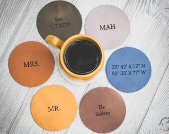 May include: Six round leather coasters with different text and colors. The coasters are arranged in a circle around a cup of coffee. The text on the coasters includes "Est. 1.7.2019", "MAH", "MRS.", "33° 42' 4.12" N 89° 33' 3.77" W", "MR.", and "The Sellers".