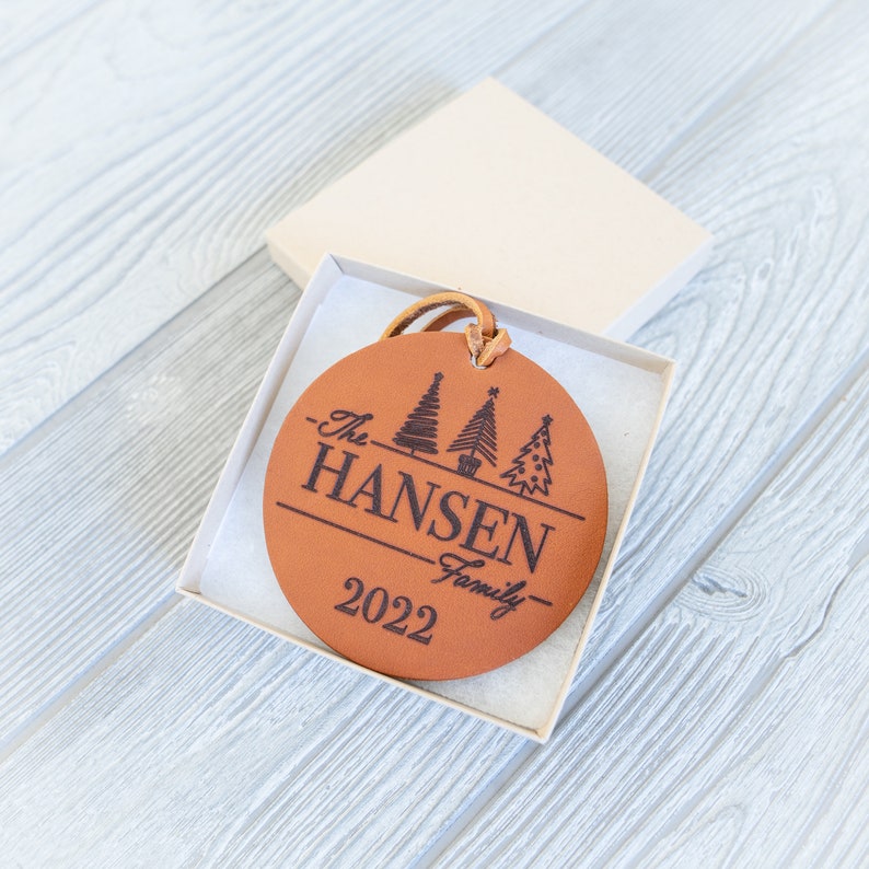 May include: A brown leather Christmas ornament with the text "The Hansen Family - 2022" and three stylized Christmas trees.
