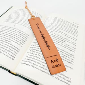 An open book with text on the pages, and a personalized leather bookmark with the text "To many men, my love, I am your partner" printed on it.