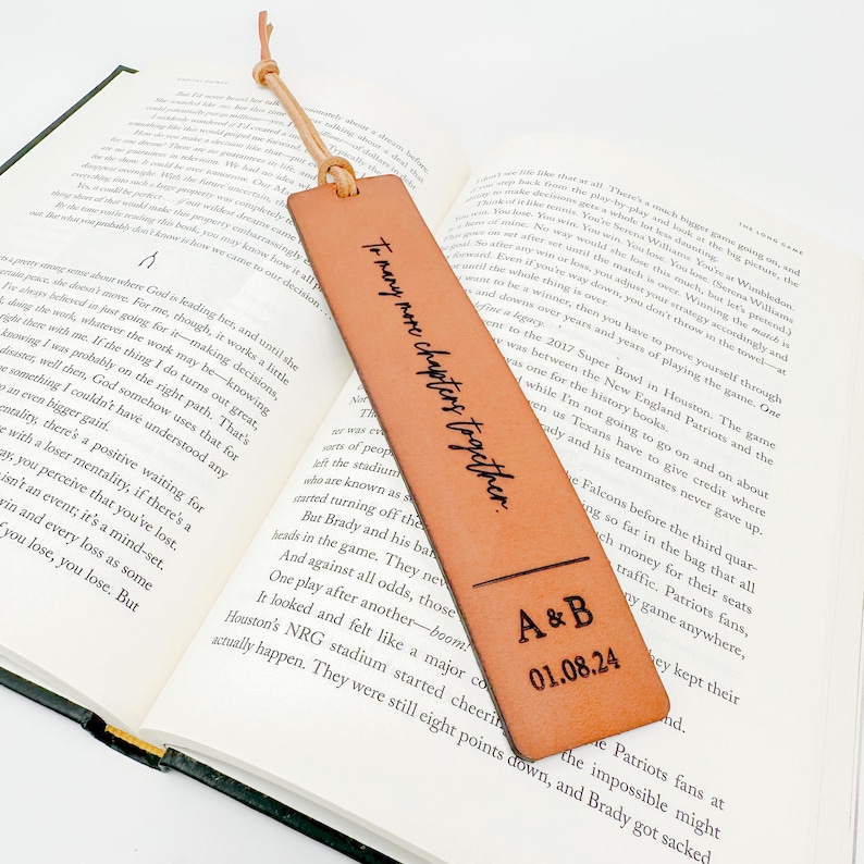 An open book with text on the pages, and a personalized leather bookmark with the text "To many men, my love, I am your partner" printed on it.