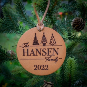 May include: A brown leather Christmas ornament with the text "The Hansen Family - 2022" and three stylized Christmas trees.