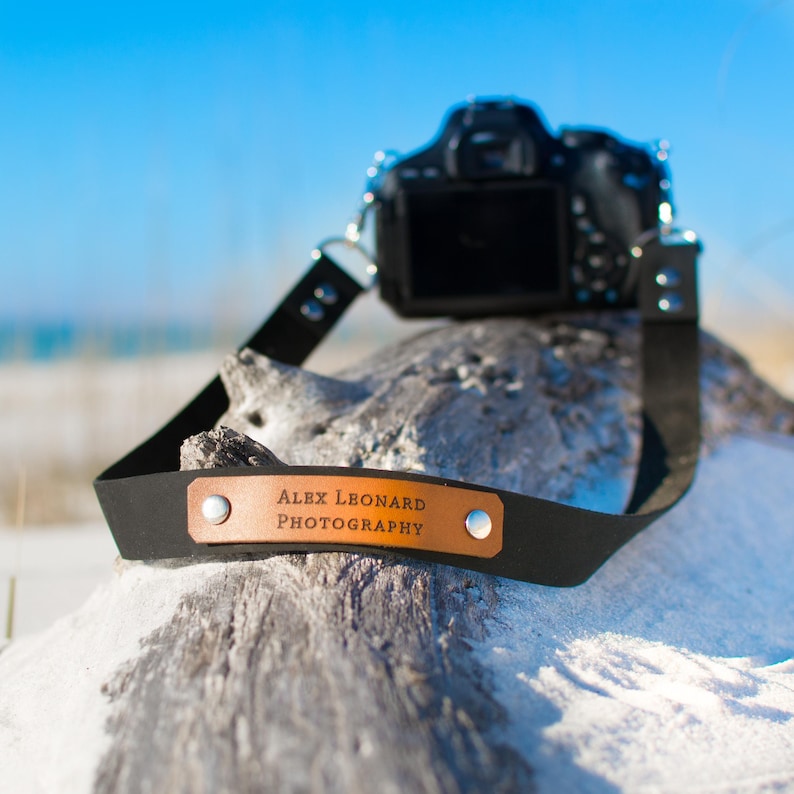 May include: A black leather camera strap with a brown leather patch that says "Alex Leonard Photography".