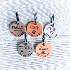 Puede incluir: Cinco chapas redondas de cuero para perros con anillos de metal. Las chapas son de color marr&oacute;n, naranja y blanco con diferentes dise&ntilde;os y texto. El texto en las chapas incluye los nombres "Wally", "Chip", "Chip", "Cooper" y "Sadie" junto con n&uacute;meros de tel&eacute;fono.