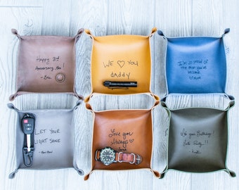 May include: Six brown leather catchall trays with different handwritten messages. The messages include "Happy 3rd Anniversary, Boo! -Eric", "WE YOU daddy", "I'm so proud of the man you've become. MOM", "LET YOUR LIGHT SHINE -Paw Pawel", "Love you Always -Jarak", and "It's your Birthday! Let's Party!! -Kustin".