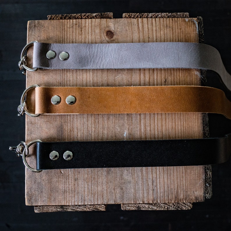 May include: Three leather straps with silver hardware and metal rings. The straps are gray, brown, and black.