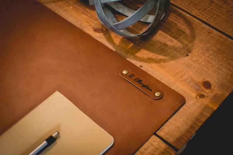 May include: A brown leather desk mat with a personalized nameplate that reads "R. Ellington". The mat is on a wooden surface.