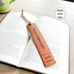 May include: A rectangular tan leather bookmark with a thin leather cord tied through a hole at the top. The bookmark features the black printed text "To many more chapters together" above the initials "A&B" and the date "01.08.24".