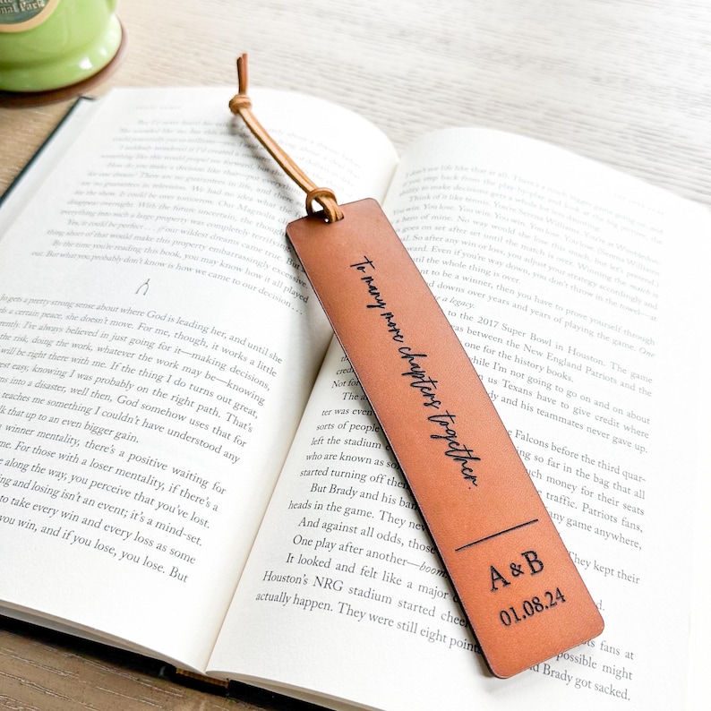 An open book with a leather bookmark featuring a personalized message, resting on a wooden surface.