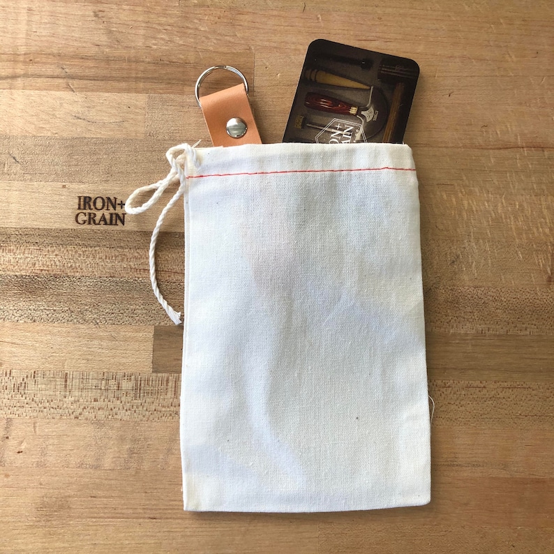 May include: A white cotton drawstring bag with a red stitch detail. A small card with the text "IRON+GRAIN" is inside the bag.