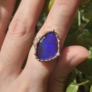 Könnte beinhalten: Ein silberner Ring mit einem großen, dunkelblauen Opal-Edelstein, der in einer strukturierten, verzierten Fassung sitzt.