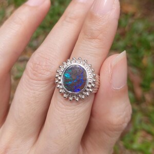 May include: A silver ring with a blue and green opal gemstone set in a beaded halo design.