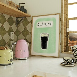 May include: A kitchen counter with a pink electric kettle, a yellow toaster, and a framed print with the word "Sl&aacute;inte" and a drawing of a glass of dark beer.