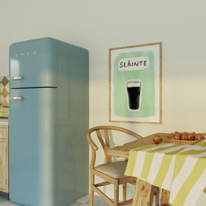 May include: A light blue retro refrigerator with the word "SMEG" on the front. A framed print with the word "Sl&aacute;inte" and a drawing of a glass of beer hangs on the wall. A wooden table with a yellow and white striped tablecloth sits in front of the refrigerator.