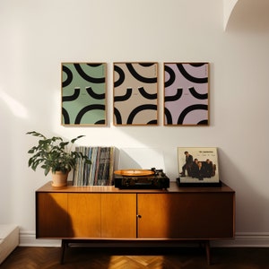 Three Guinness prints on the wall above a cranberries vinyl. Irish art with abstract guinness art showing wiggley pint glasses on beige, green and pink backgrounds.a great christmass gift for any guinness lover